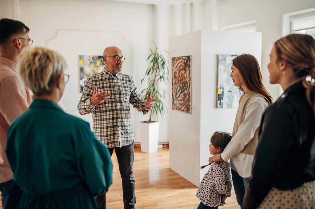 A photograph of a male artist in meaningful social dialogue art review with a diverse group at a participant location.